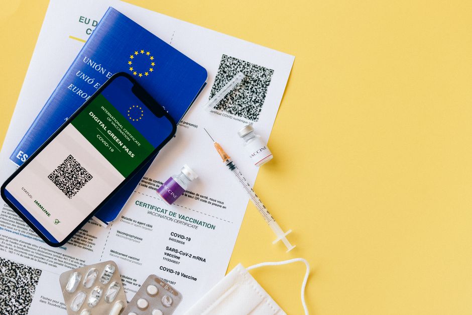 Pasaporte de vacuna digital y elementos de vacunación COVID-19 incluyendo jeringas y máscaras sobre un fondo amarillo.