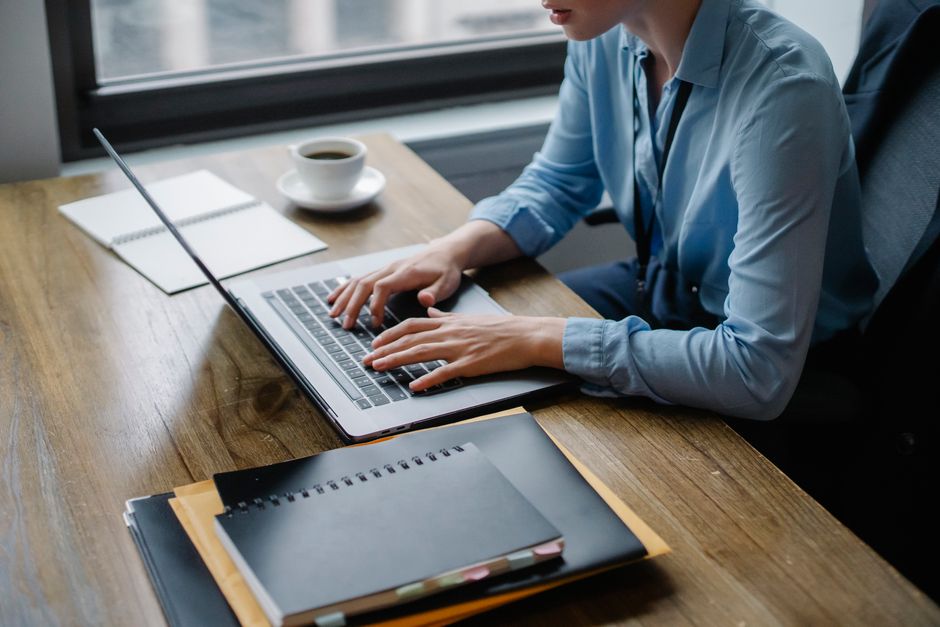 Trabajador de oficina escribiendo en laptop con café y cuadernos en el escritorio, capturando un entorno de trabajo enfocado.