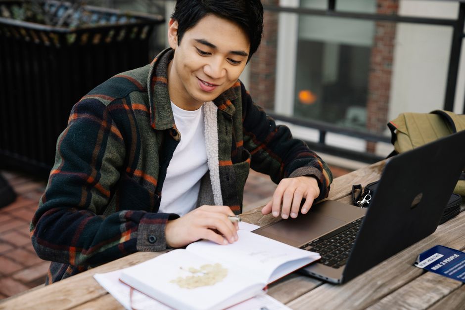 Hombre adulto estudiando al aire libre usando una laptop y un cuaderno en una mesa de madera. Concepto de educación.