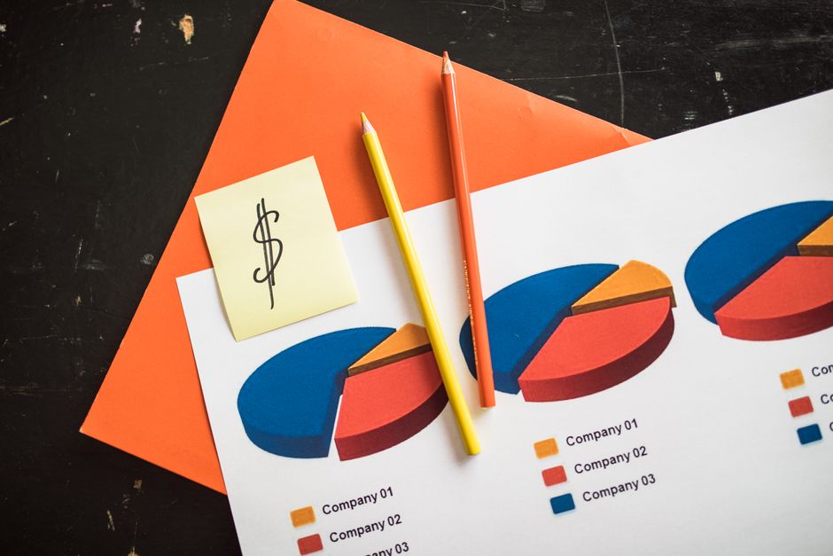 Una disposición creativa de gráficos de pastel financieros con lápices coloridos y un billete de dólar, perfecto para temas de negocios.