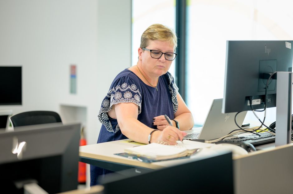 Mujer profesional con gafas trabajando en un escritorio con una computadora portátil y un cuaderno.