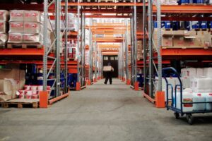 Un trabajador llevando una caja en un pasillo de almacenamiento bien organizado.